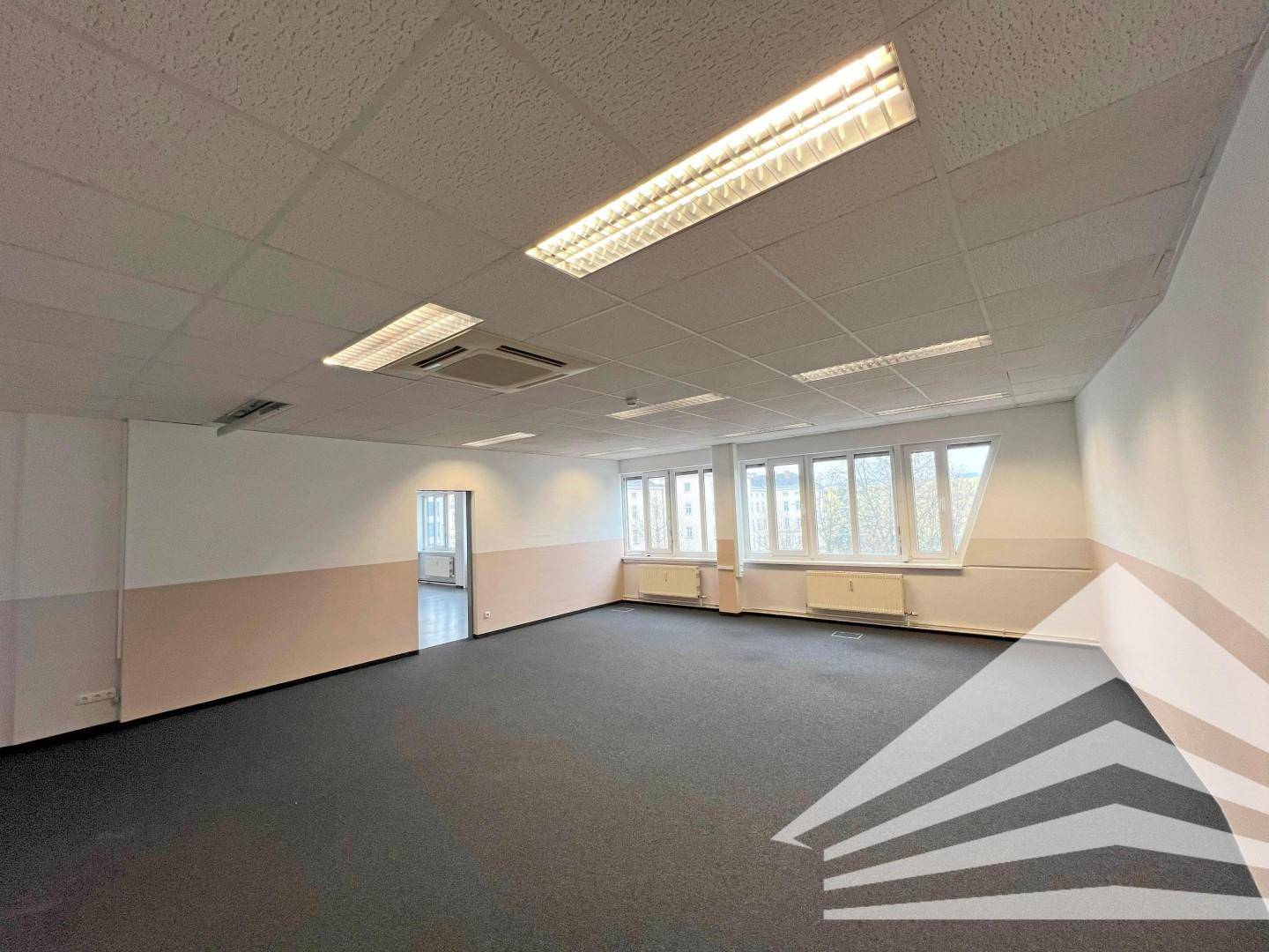 Großes, leeres Büro mit dunklem Teppichboden, abgehängter Decke und Fenstern, ideal für Büronutzung.