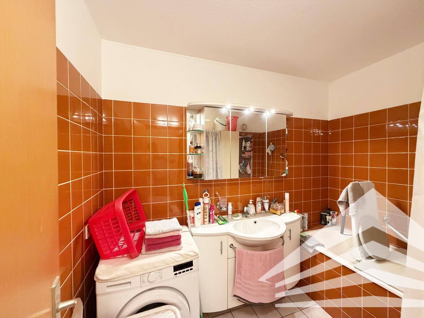 Badezimmer mit orangefarbenen Fliesen, Badewanne, Waschbecken und Waschmaschine.