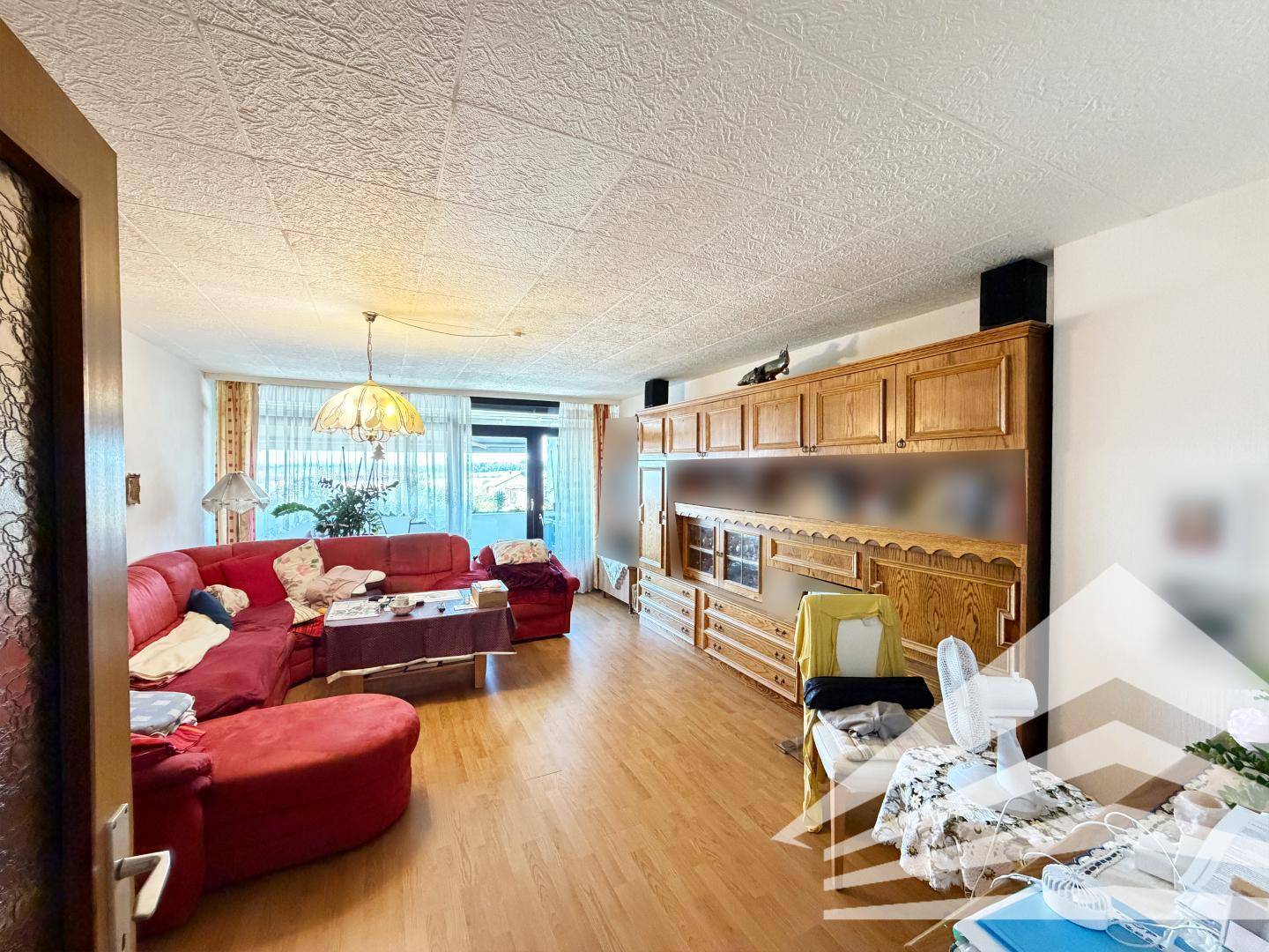 Geräumiges Wohnzimmer mit traditionellen Holzmöbeln, rotem Sofa und strukturierten Deckenplatten.