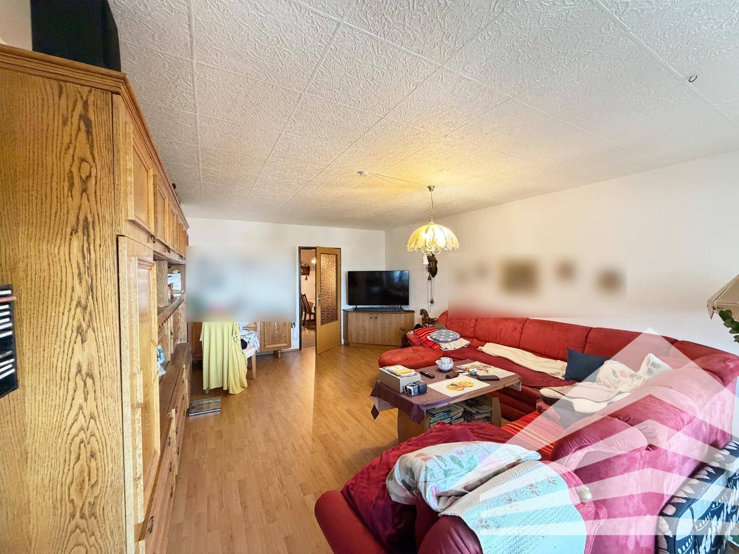 Gemütliches Wohnzimmer mit rotem Ecksofa, Holzschrankwand und Blick auf den Flur.