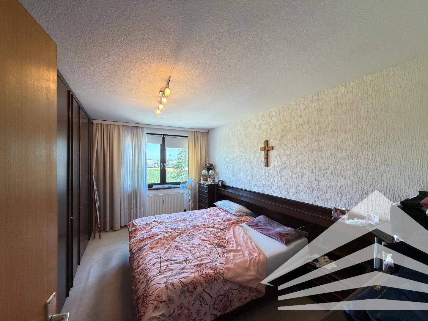 Schlafzimmer mit Doppelbett, Holzschrank und Fenster mit Blick ins Grüne.