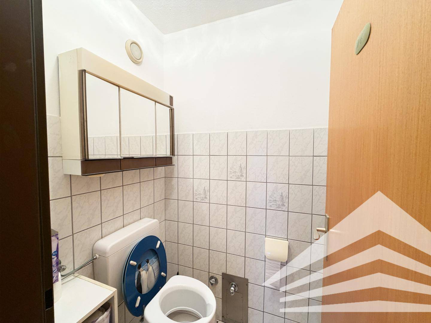 Separates WC mit hellen Fliesen, Toilette und Spiegelschrank.