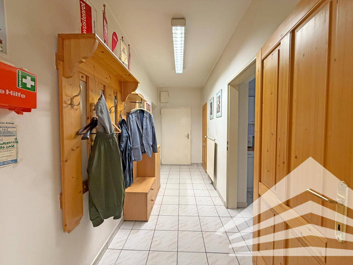 Langer Flur mit Fliesenboden, Holzvertäfelung und Garderobe, führt zu weiteren Räumen.