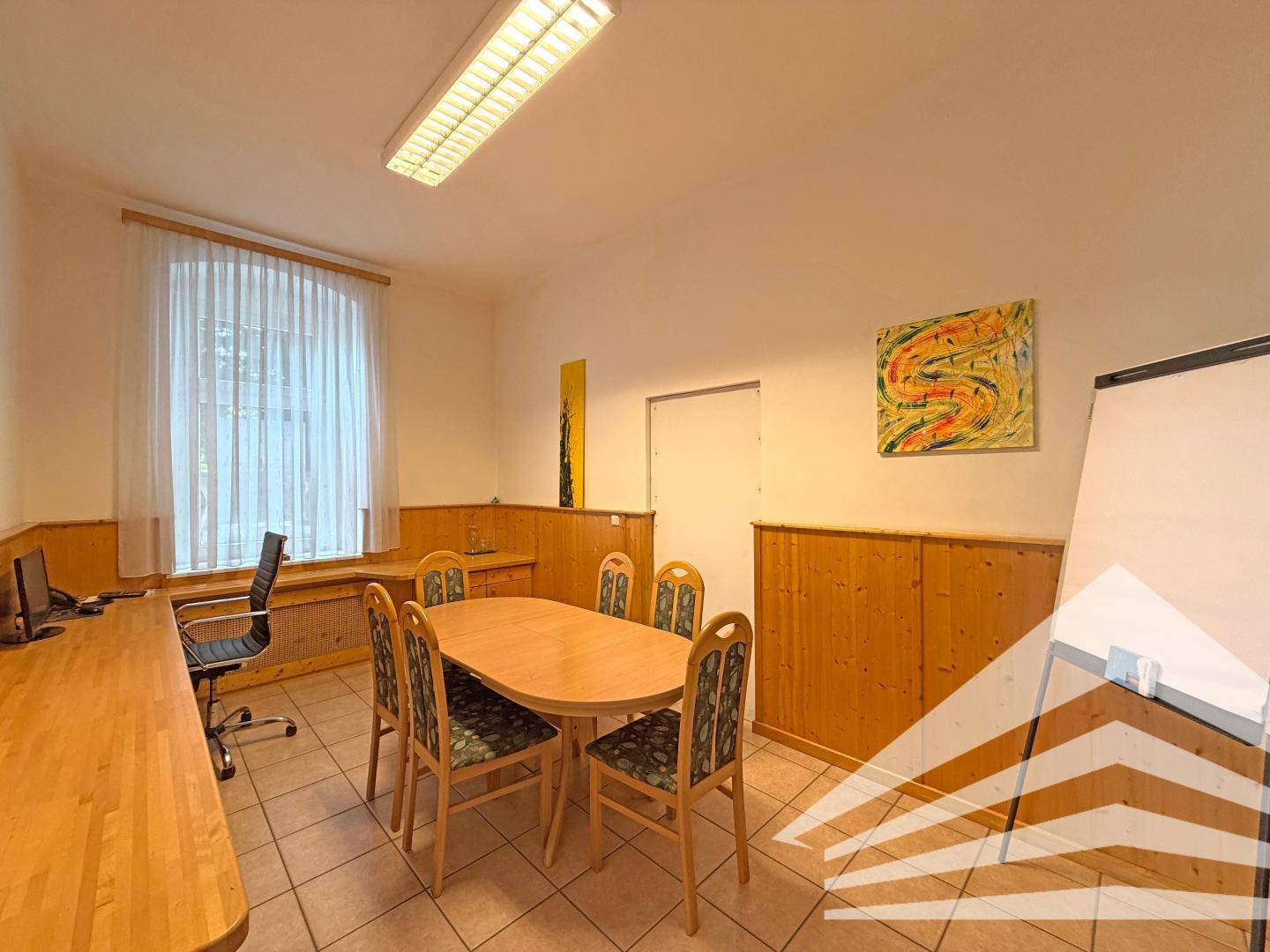 Besprechungsraum mit großem Holztisch, Stühlen und einem Fenster mit Vorhängen, ideal für Meetings.