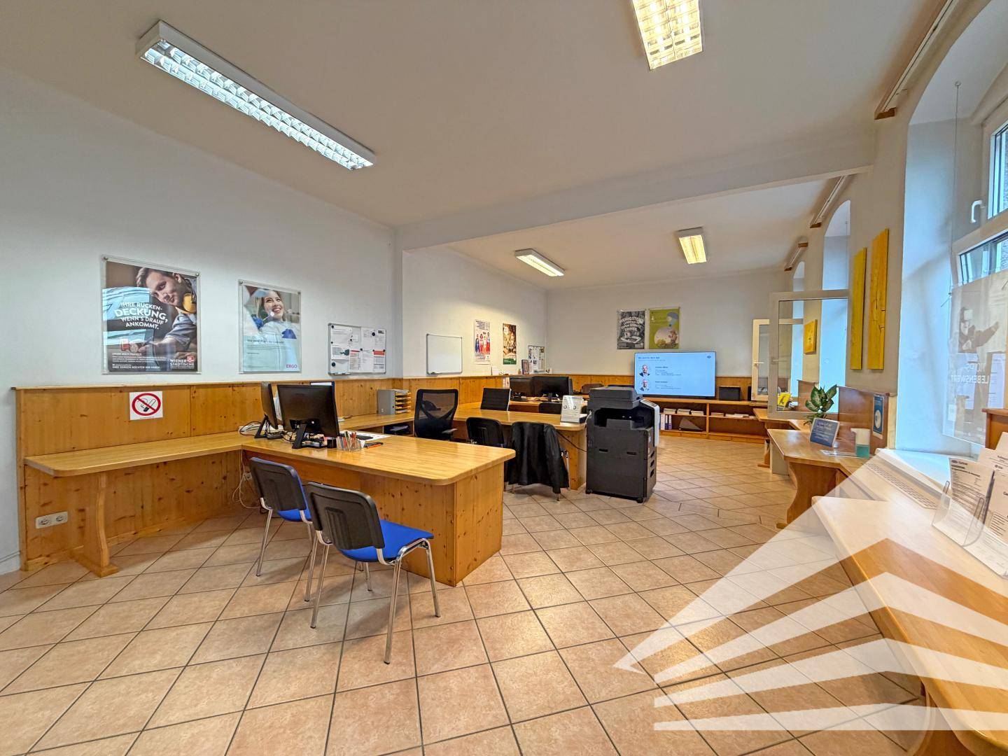 Großes Büro mit mehreren Arbeitsplätzen, Holzmöbeln und Fliesenboden, gut beleuchtet und funktional.