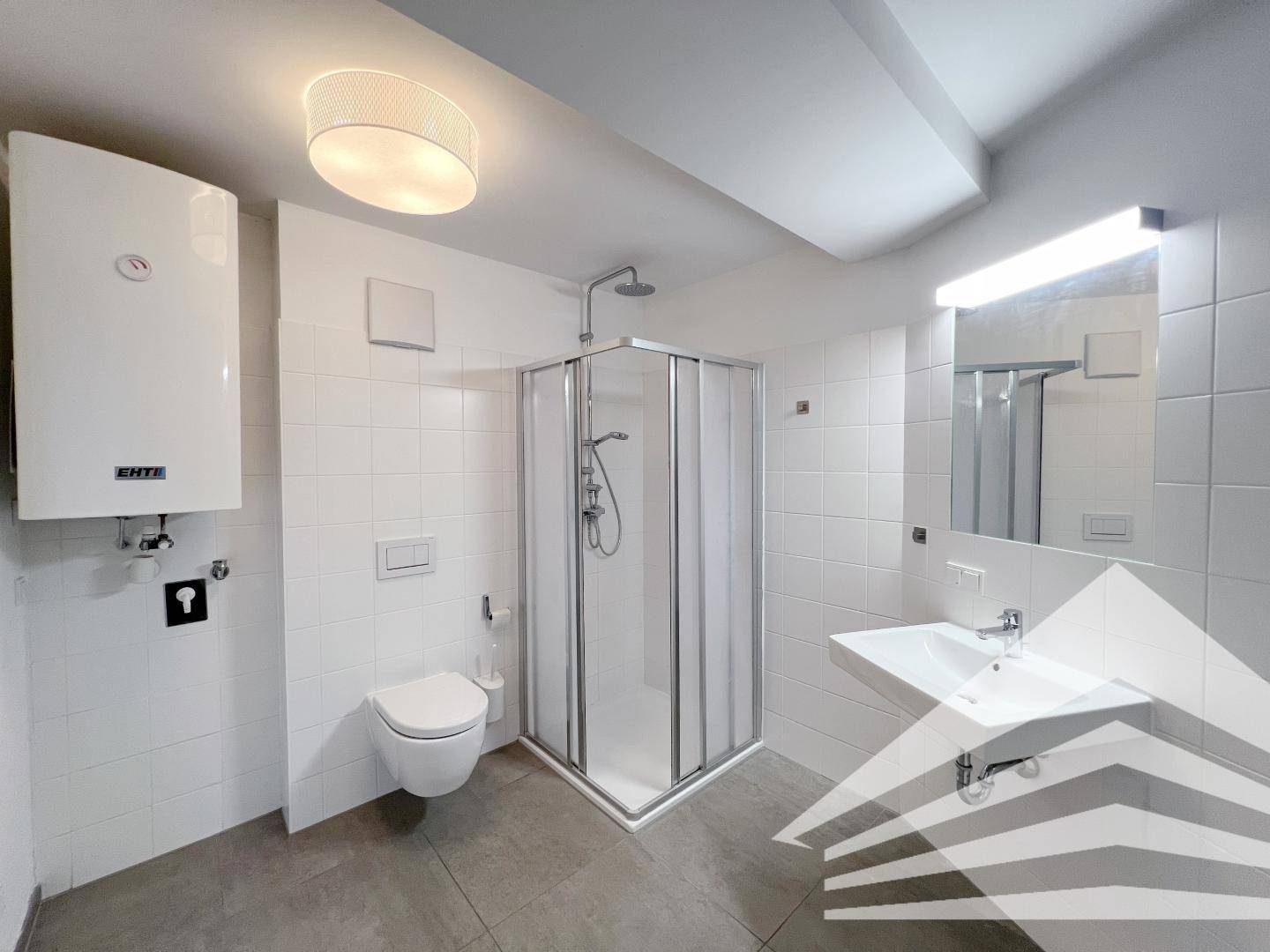 Helles Badezimmer mit weißen Fliesen, Dusche, WC und Waschbecken, ausgestattet mit einem Warmwasserbereiter.
