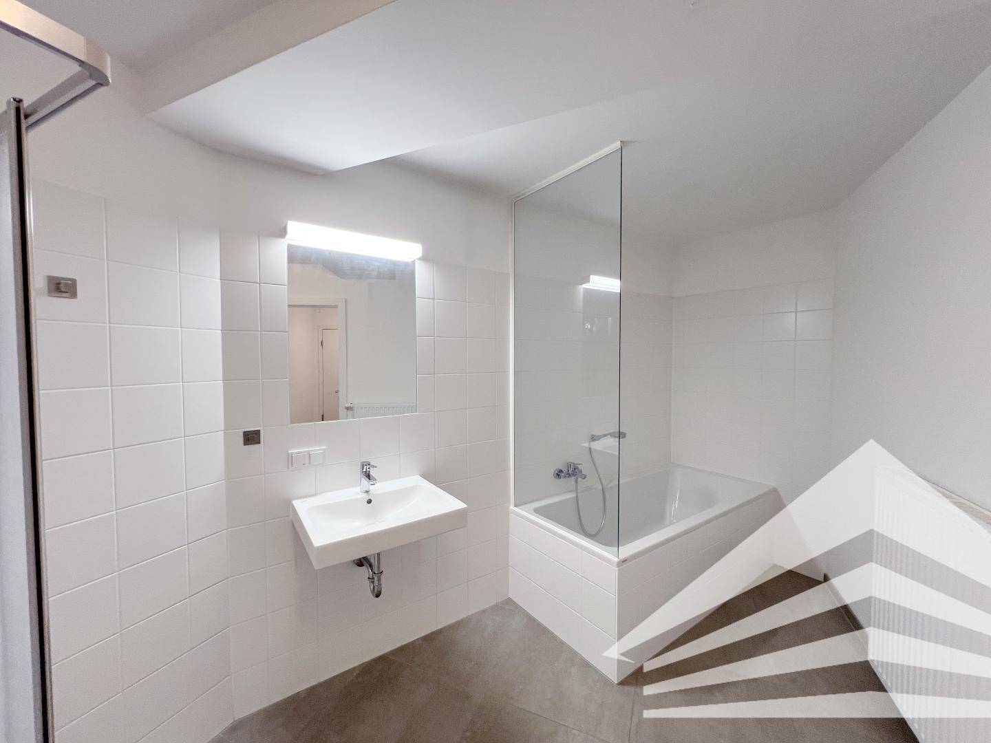 Modernes Badezimmer mit weißen Fliesen, Badewanne mit Glasabtrennung und Waschbecken.