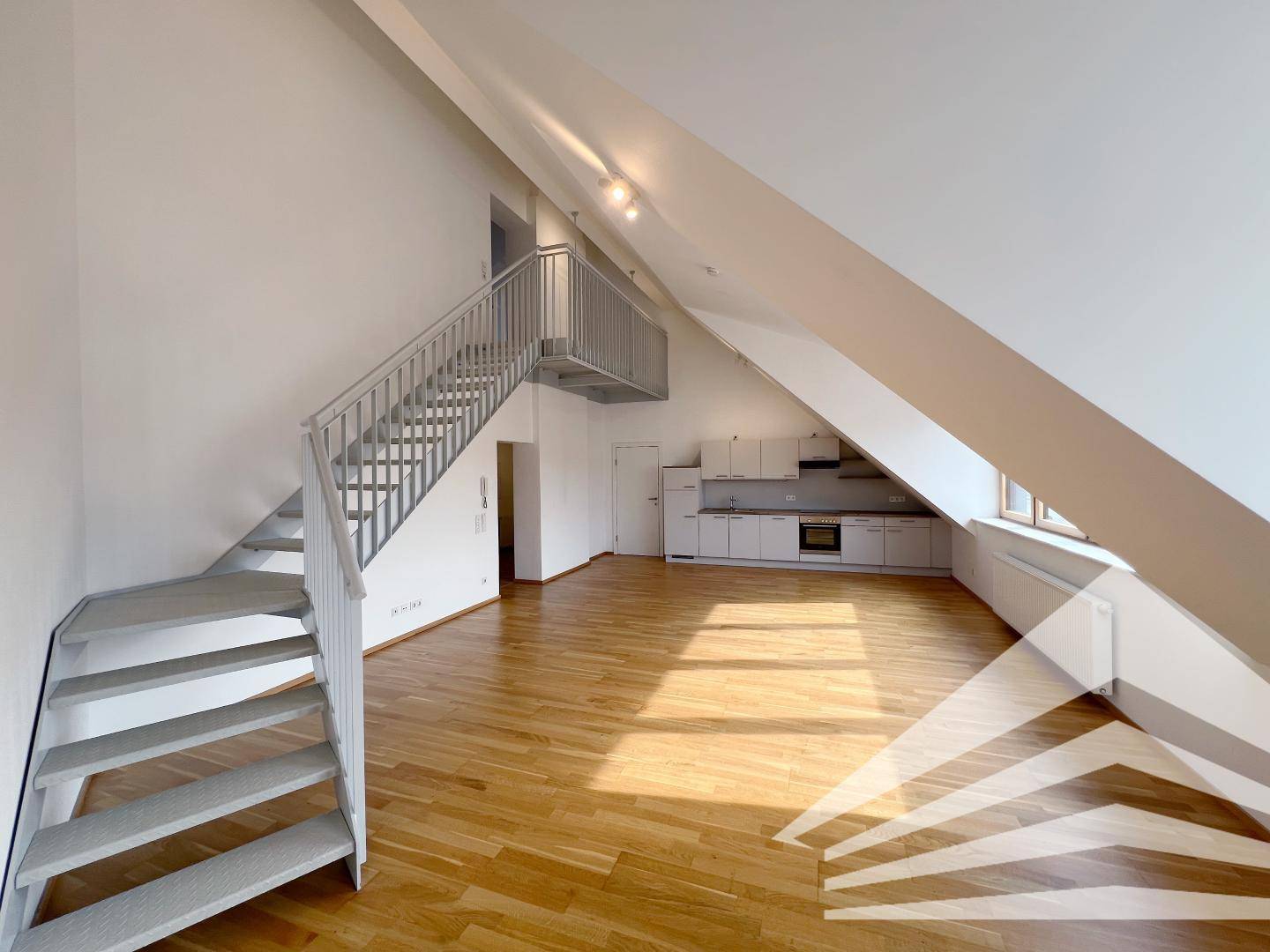 Heller offener Wohnbereich mit Holzboden, Dachschrägen und integrierter Küchenzeile sowie einer Treppe zur Galerie.