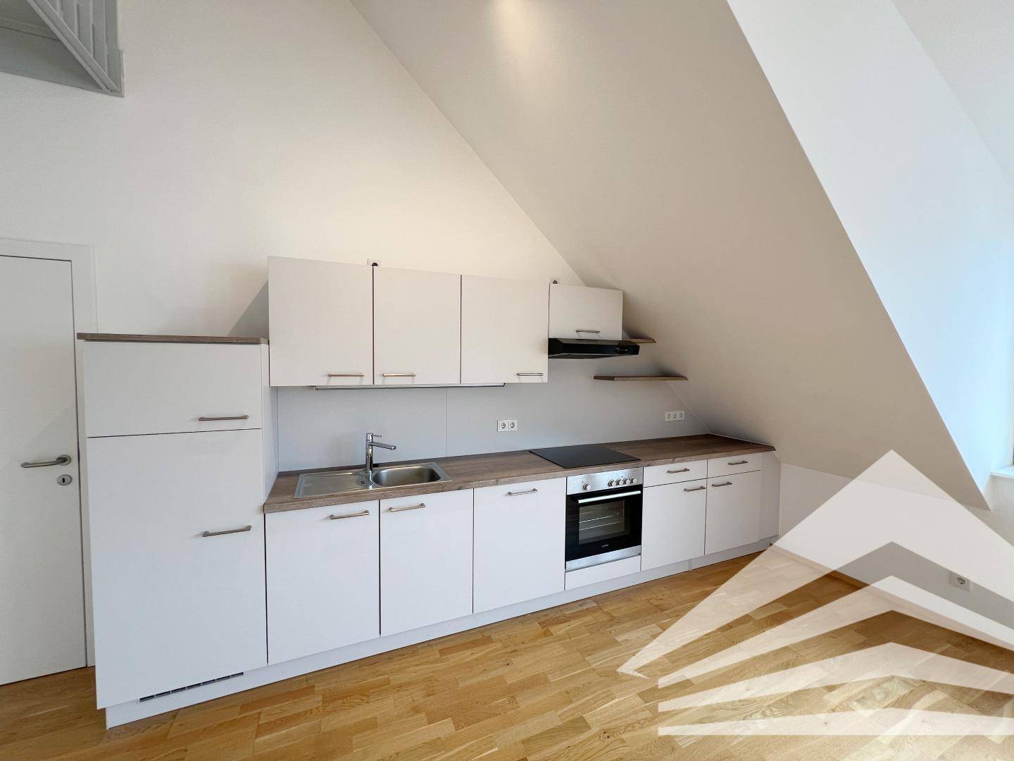 Funktionale Küchenzeile mit weißen Schränken, Holz-Arbeitsplatte und integrierten Geräten unter der Dachschräge.