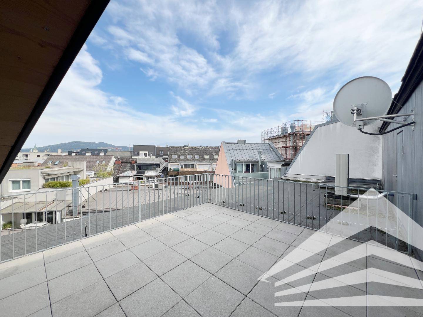Weitläufige Dachterrasse mit Metallgeländer und Panoramablick über die Dächer der Stadt.