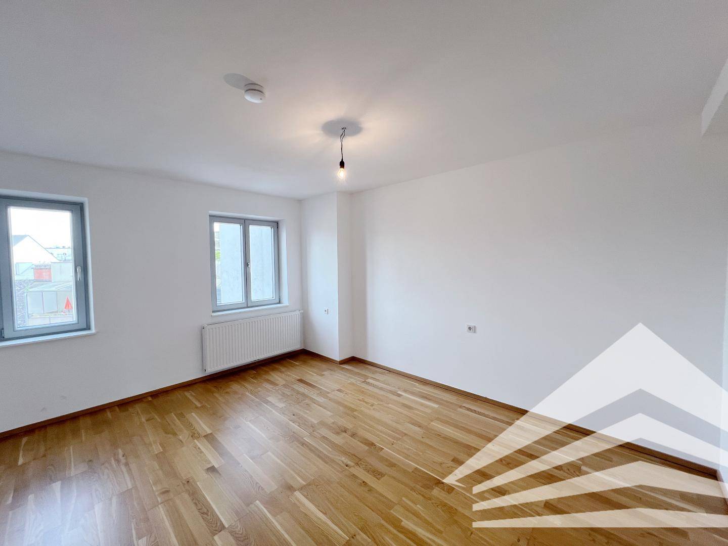 Helles Schlafzimmer mit Holzboden, weißen Wänden und zwei Fenstern für natürliche Belichtung.