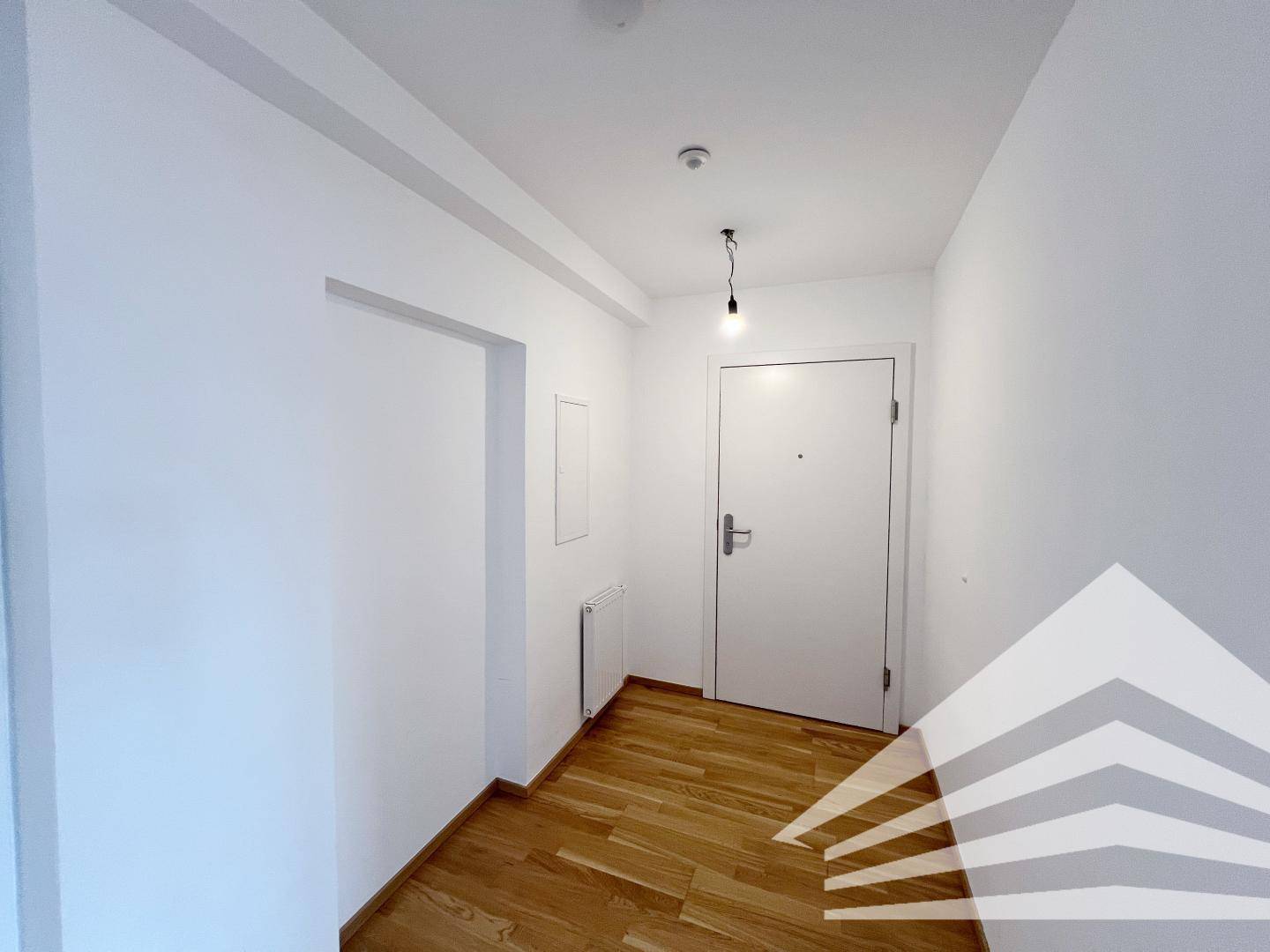 Heller Eingangsbereich mit Holzboden und weiß gestrichenen Wänden, der zur Wohnungstür führt.