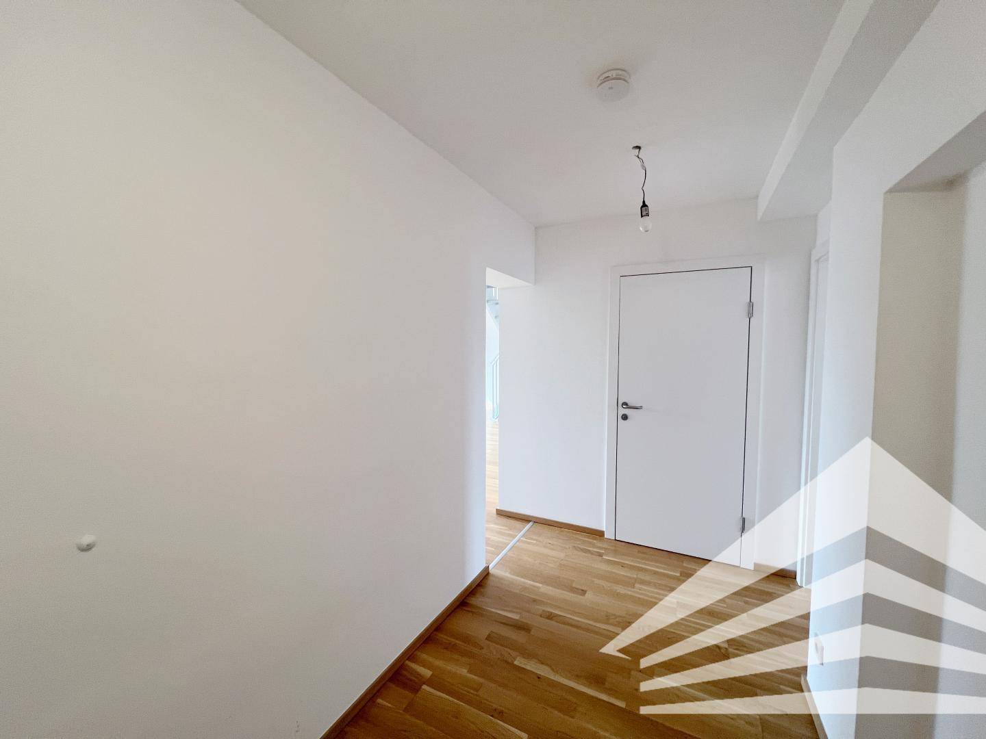 Langer Flur mit Holzboden und weißen Wänden, der die verschiedenen Räume der Wohnung verbindet.
