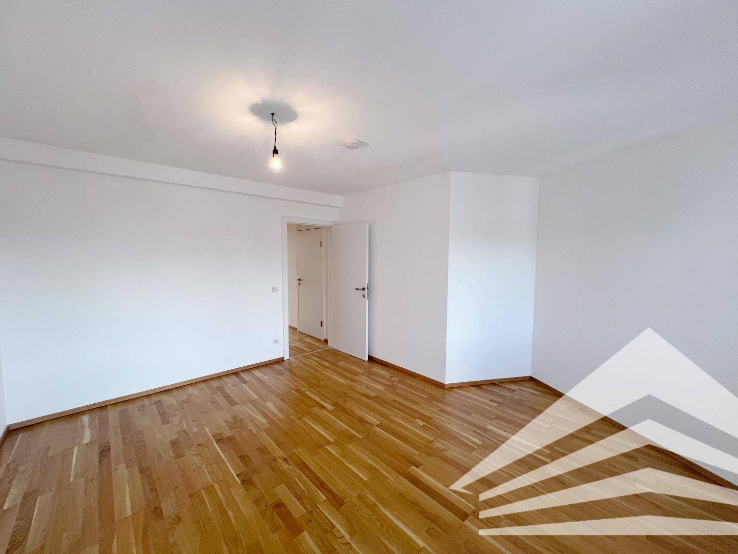 Geräumiges Schlafzimmer mit Holzboden und Zugang zu einem weiteren Raum oder Flur.