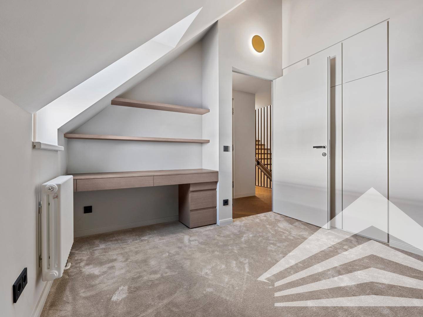 Helles Arbeitszimmer mit Dachschräge, integriertem Schreibtisch und Teppichboden.