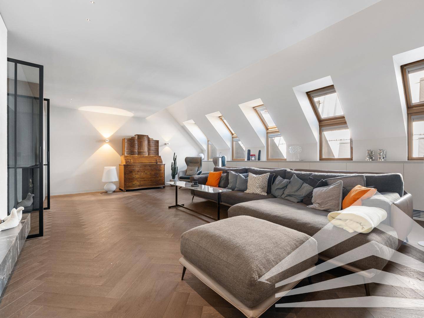 Gemütliches Wohnzimmer mit großem Ecksofa, Dachfenstern und elegantem Fischgrätparkett.