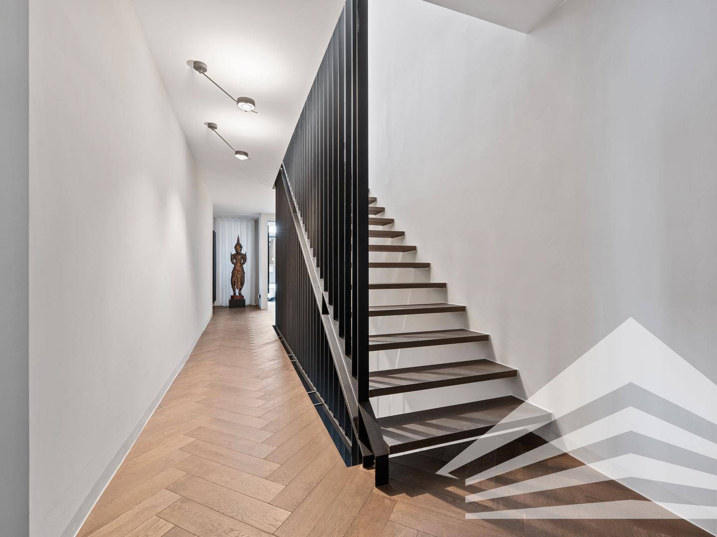 Langer Flur mit Fischgrätparkett und moderner Holztreppe, führt zu weiteren Räumen.