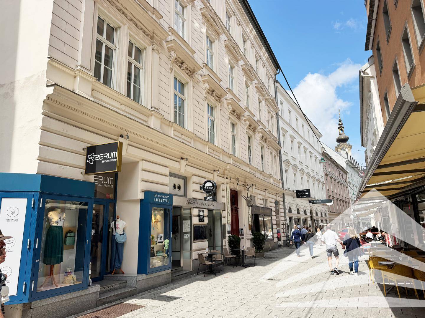 Historische Gebäudezeile in einer belebten Stadtstraße mit Geschäften und Cafés.