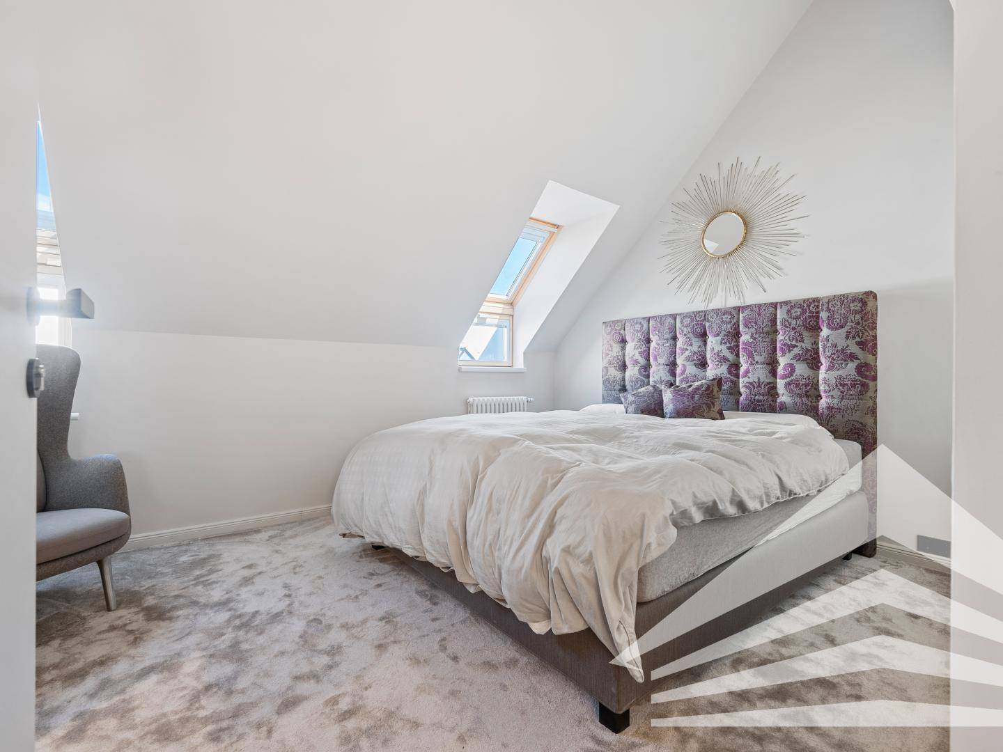 Helles Schlafzimmer mit Dachschräge, Teppichboden und großem Bett mit gepolstertem Kopfteil.