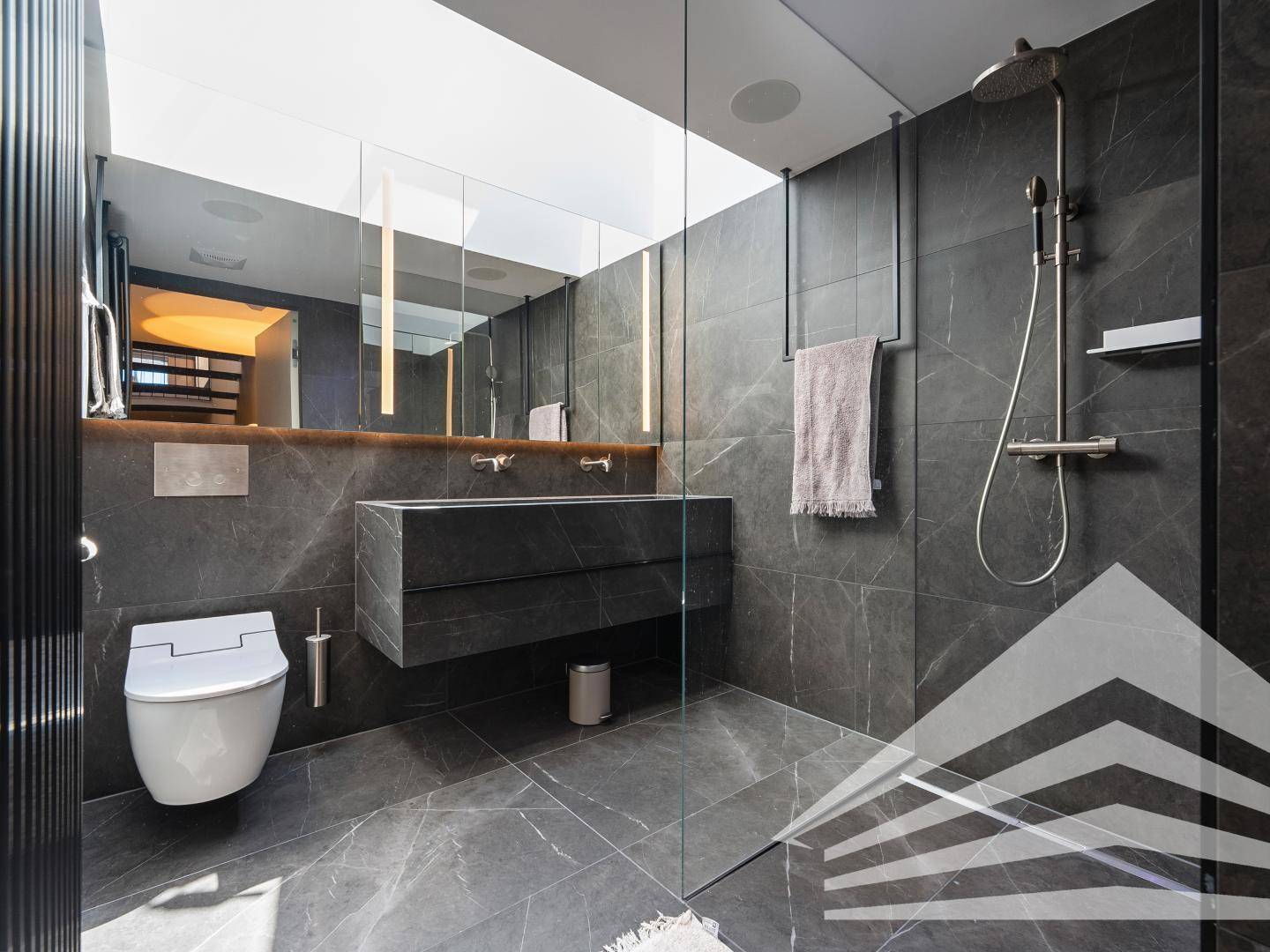 Luxuriöses Badezimmer mit großer begehbarer Dusche, Doppelwaschbecken und dunklen Fliesen.