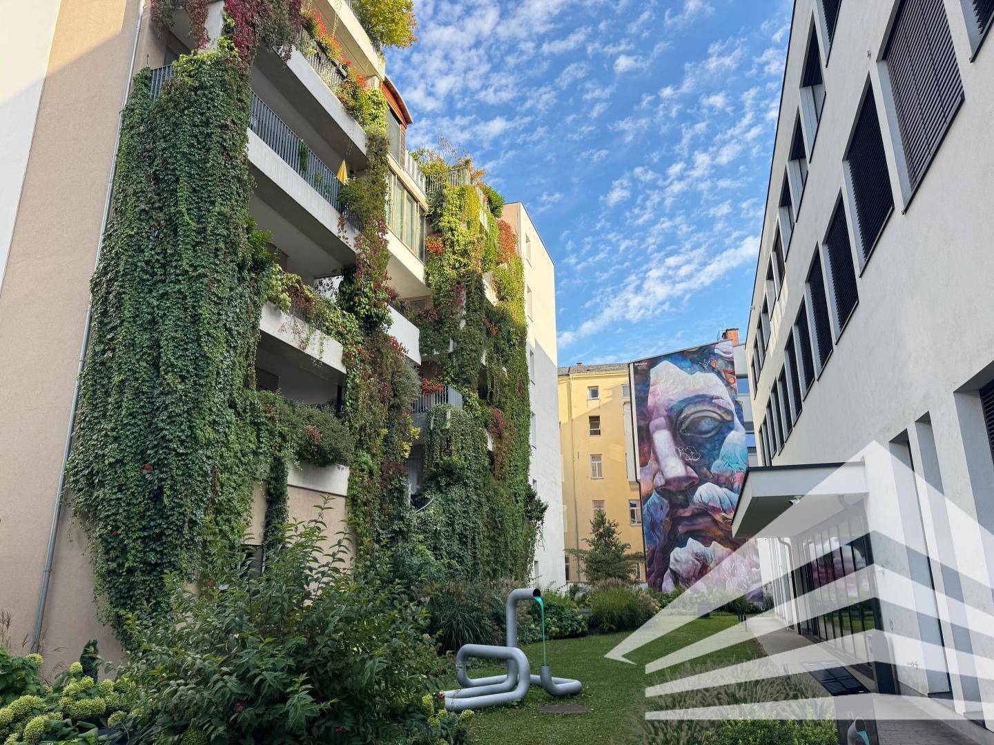 Grüne Fassade eines modernen Gebäudes mit vertikalem Garten und Kunstinstallation im Hof.