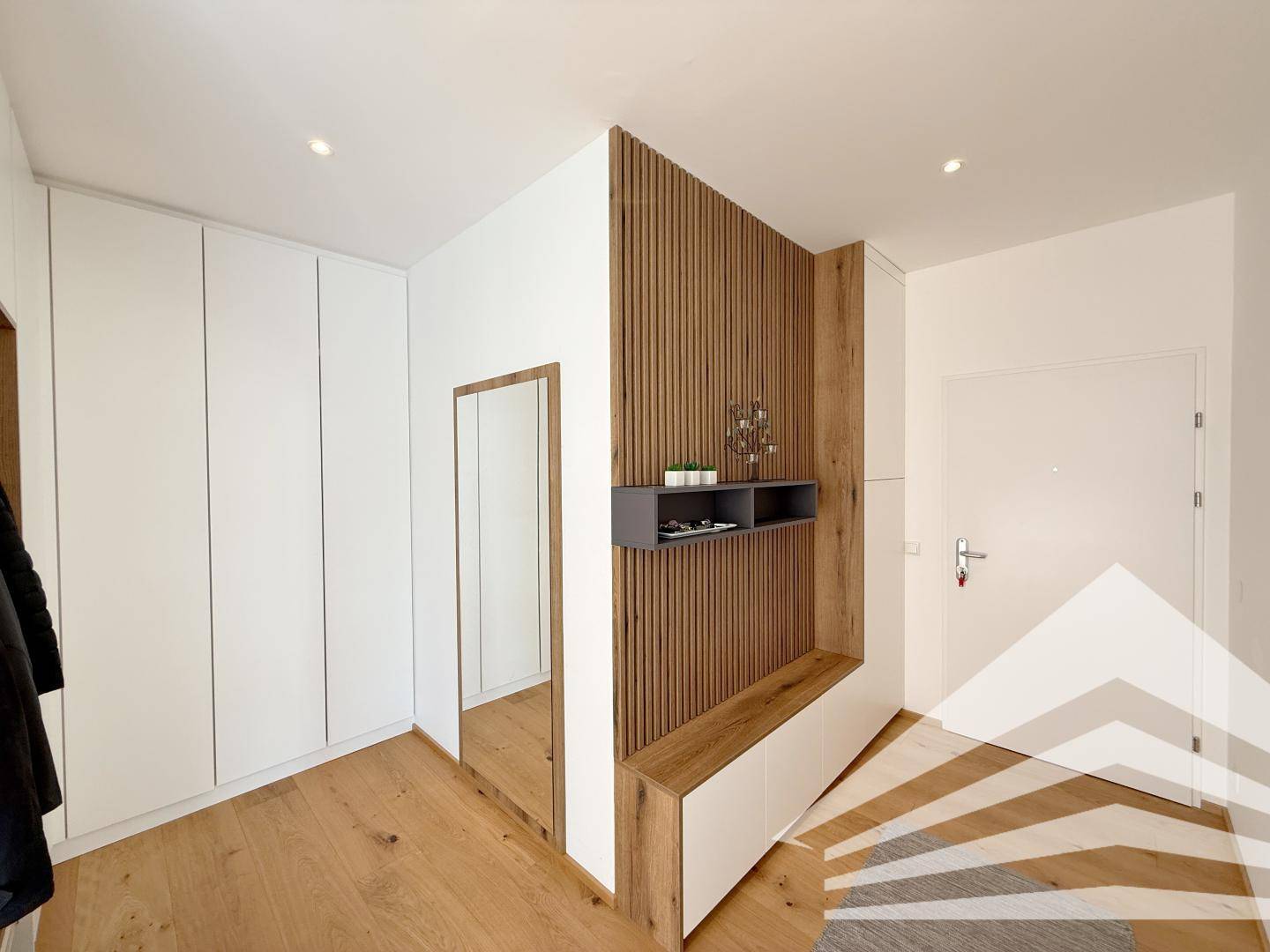 Heller Flur mit Holzboden, Einbauschränken und einem großen Spiegel.