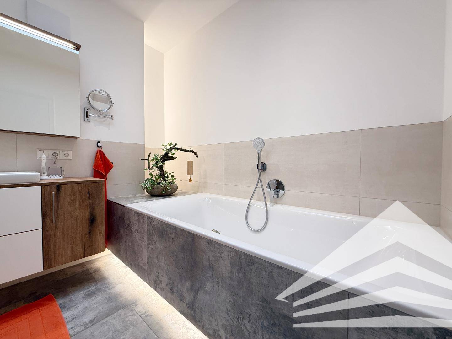 Elegantes Badezimmer mit Badewanne, Holzwaschtisch und indirekter Beleuchtung.