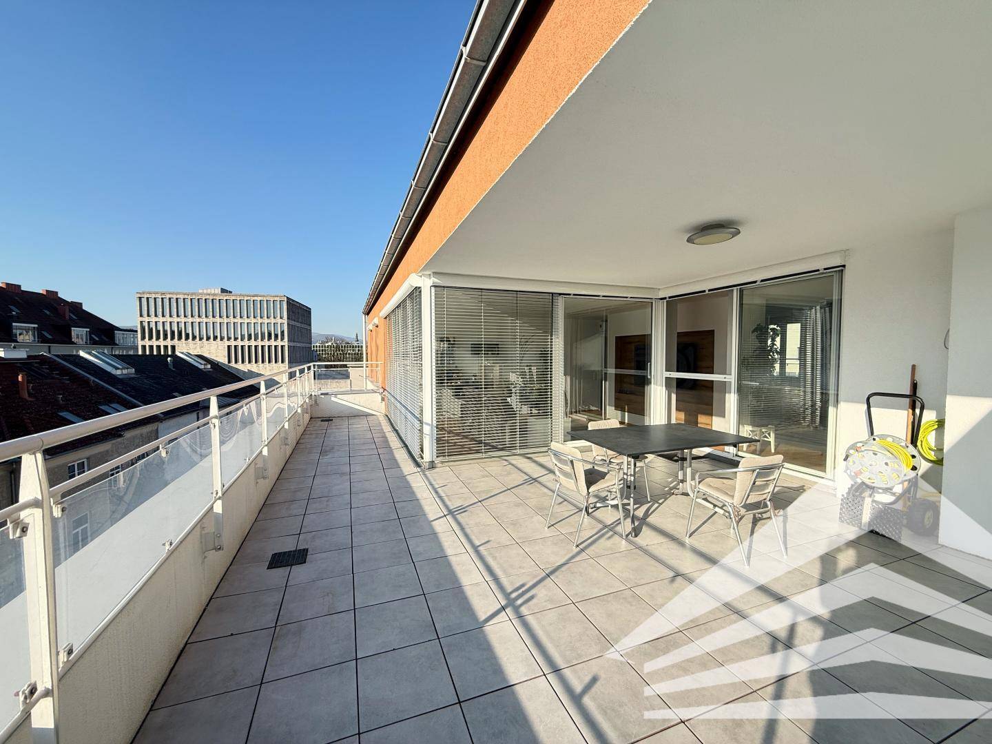 Große, sonnige Dachterrasse mit Fliesenboden, Sitzgelegenheiten und Blick auf die Stadt.