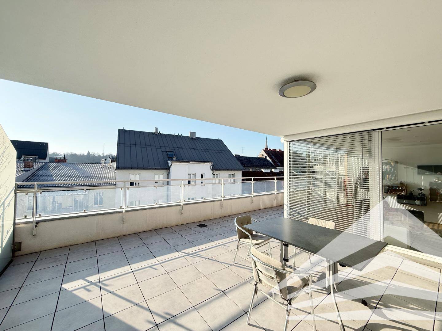 Überdachte Terrasse mit Fliesenboden und Sitzgelegenheiten, bietet Schutz vor Sonne und Regen.