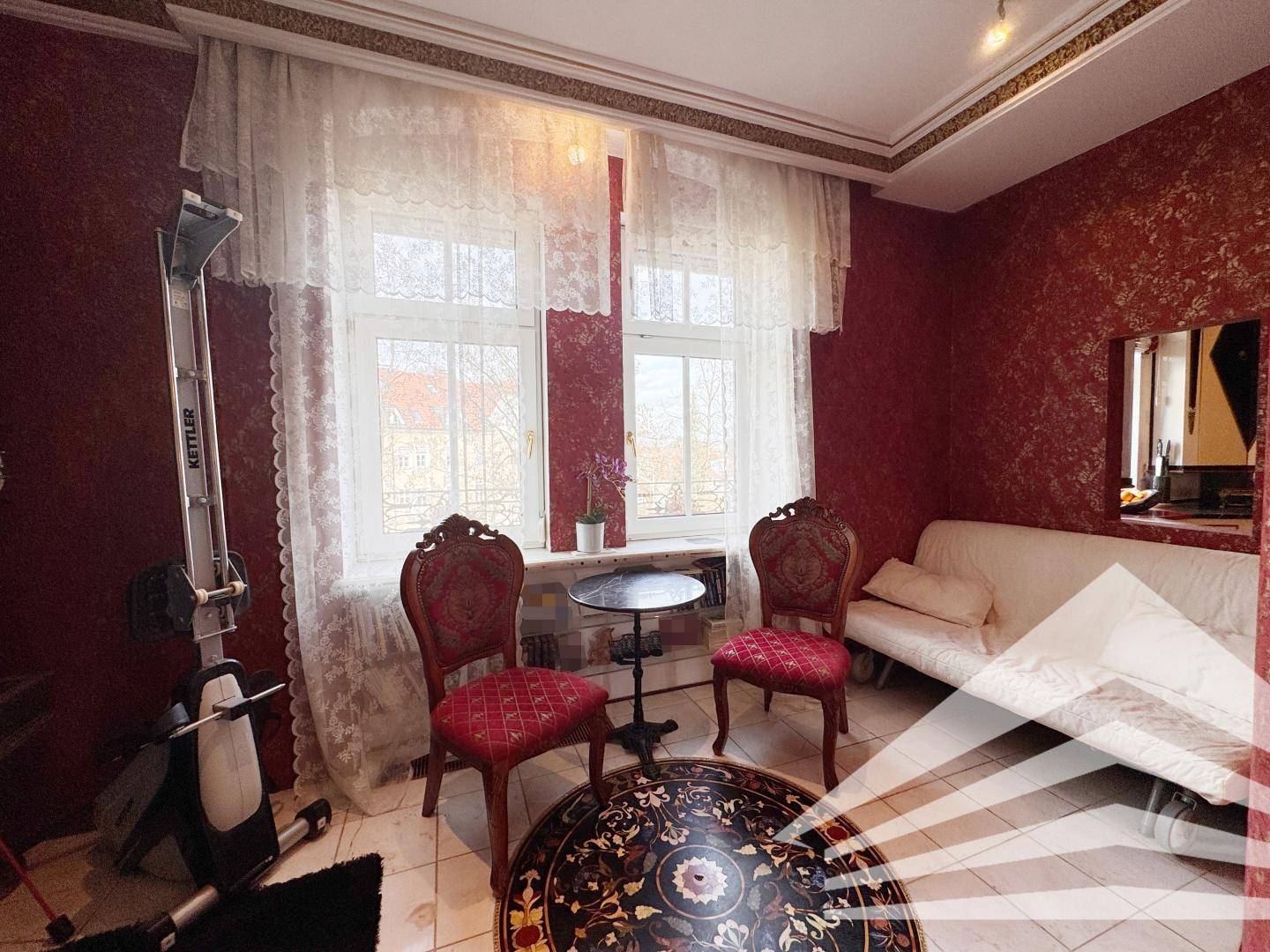 Schlafzimmer mit roter Tapete, klassischem Mobiliar und einem Heimtrainer am Fenster.