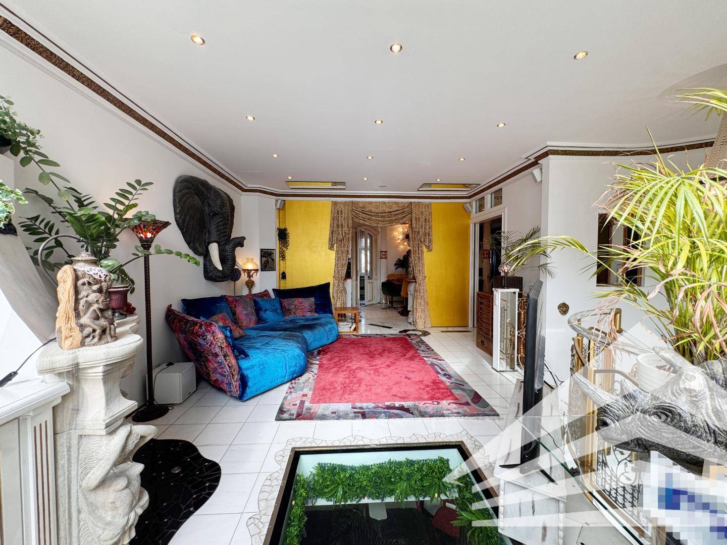 Helles Wohnzimmer mit blauer Couch, vielen Pflanzen und einem Glasboden-Element.