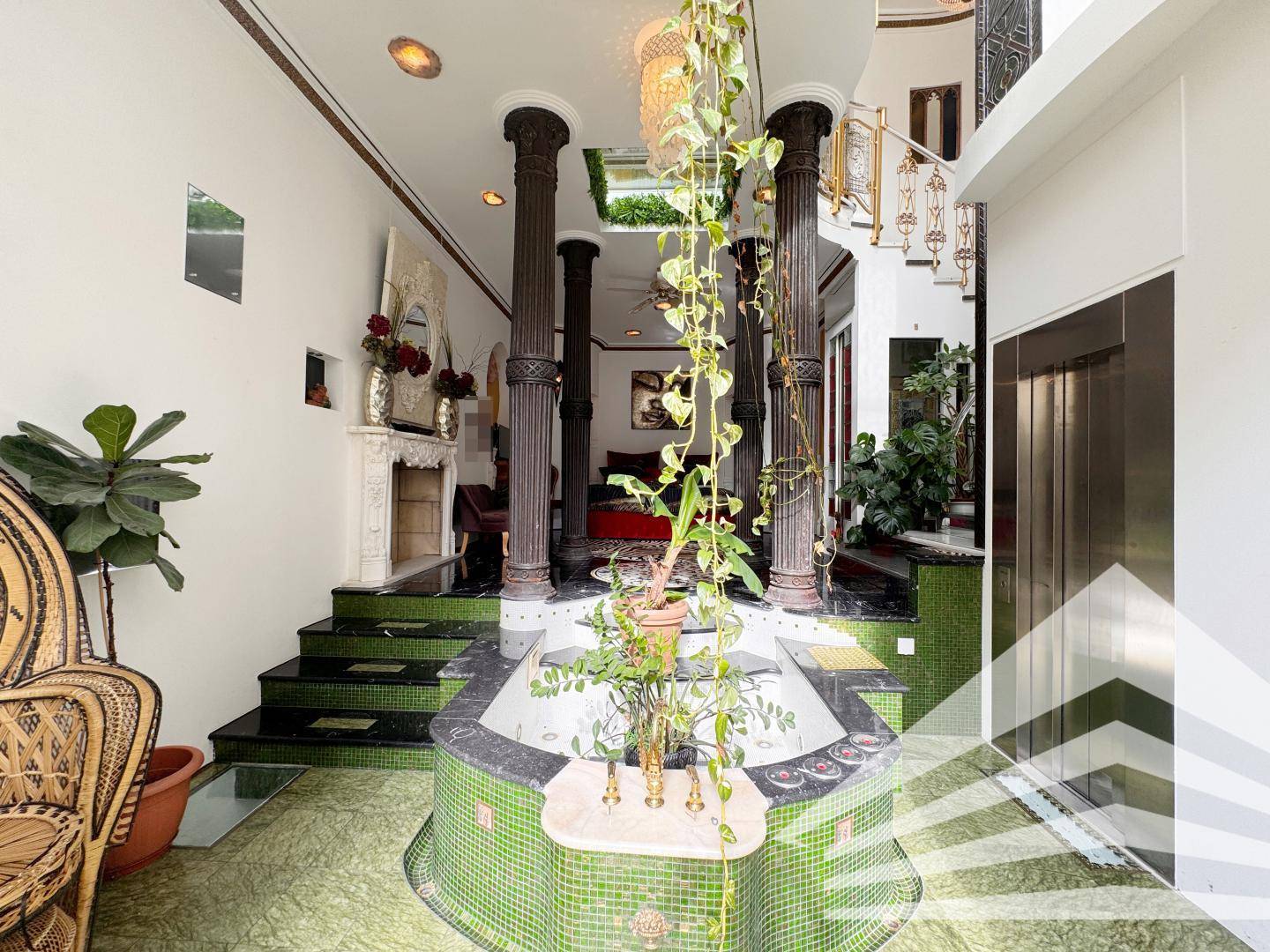 Prunkvoller Eingangsbereich mit Zierbrunnen, dunklem Marmorboden und Zugang zum Aufzug.