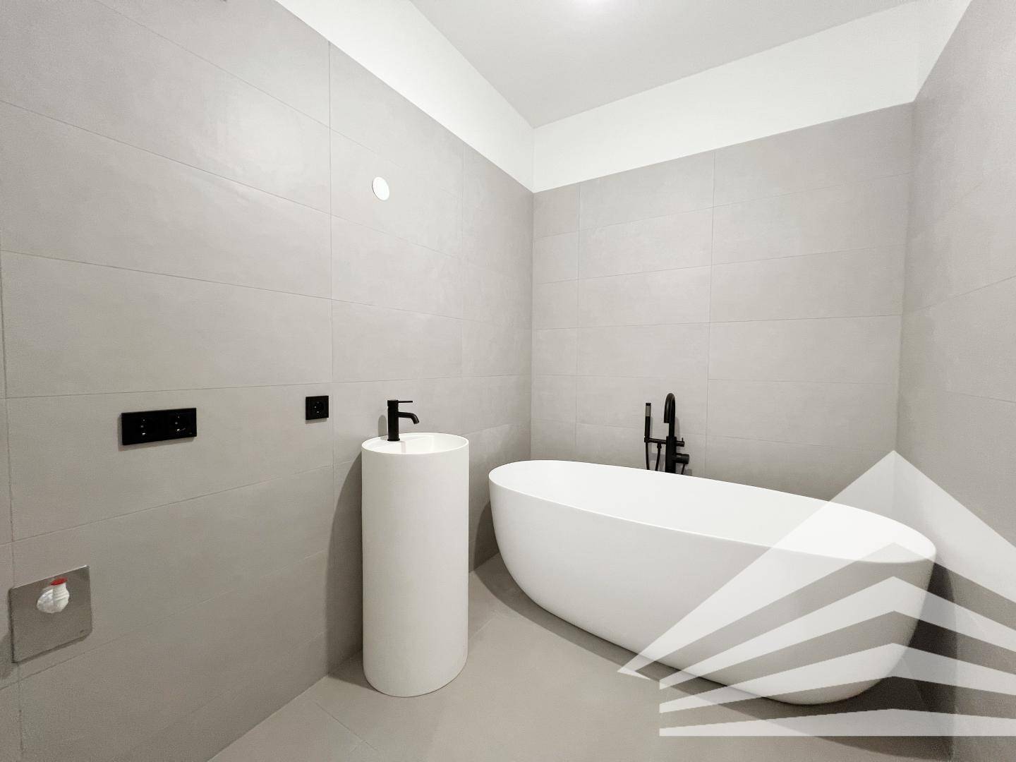 Modernes Badezimmer mit freistehender Badewanne und stilvollem Säulenwaschbecken.