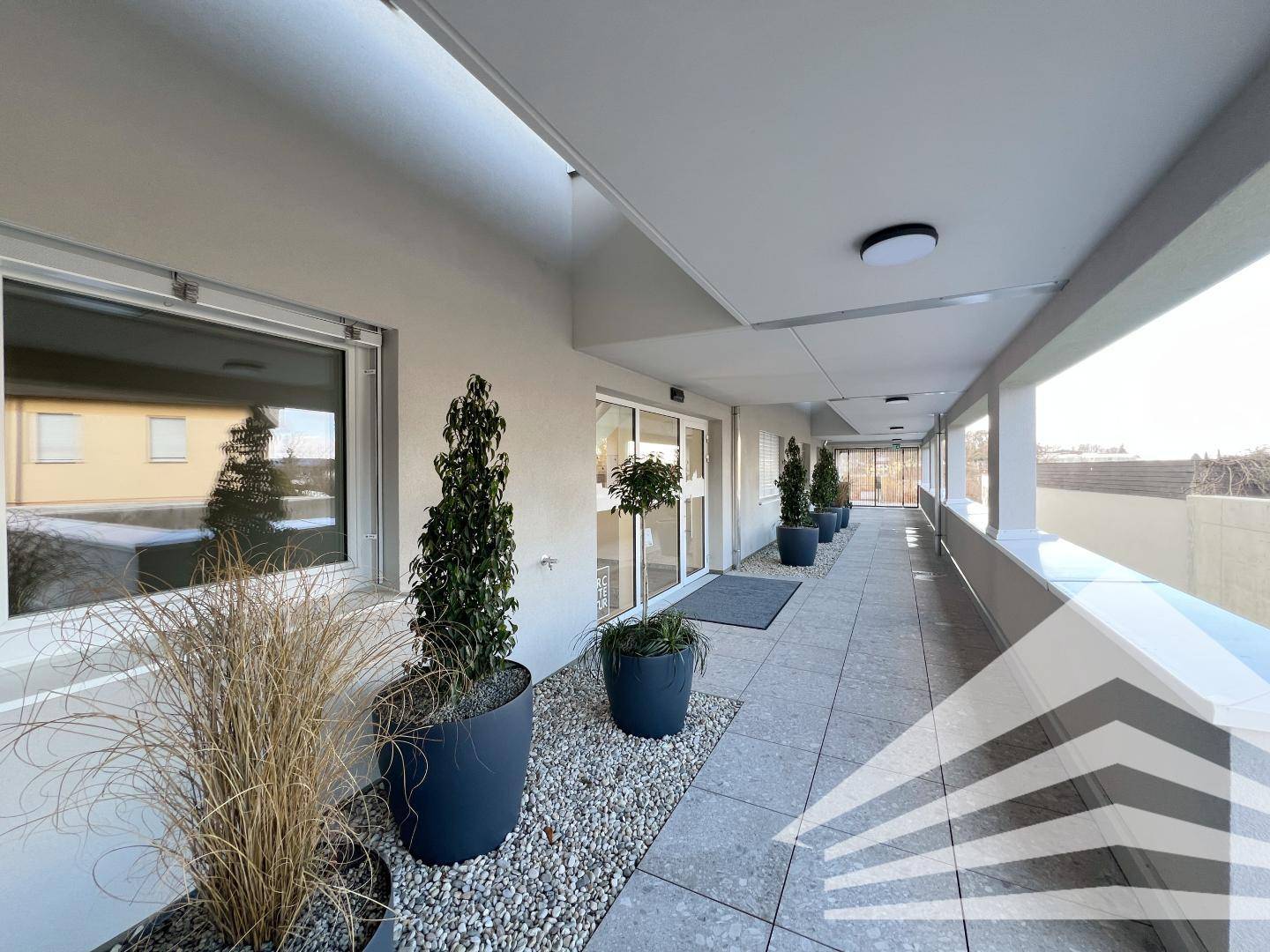 Langer überdachter Gang oder Loggia mit modernen Fliesen und dekorativen Pflanzen.