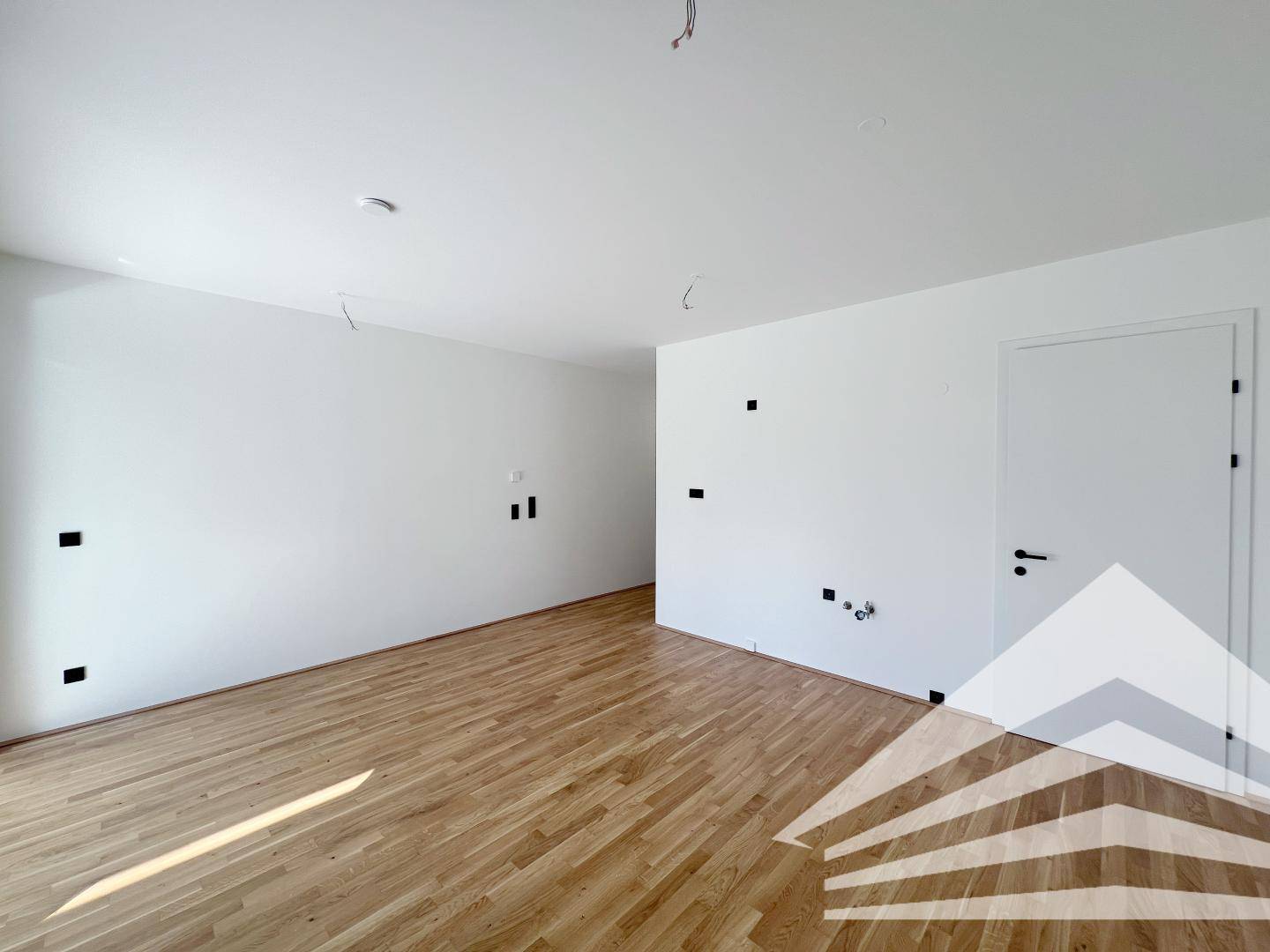 Geräumiger, unmöblierter Wohnraum mit hellem Holzboden und weißen Wänden.
