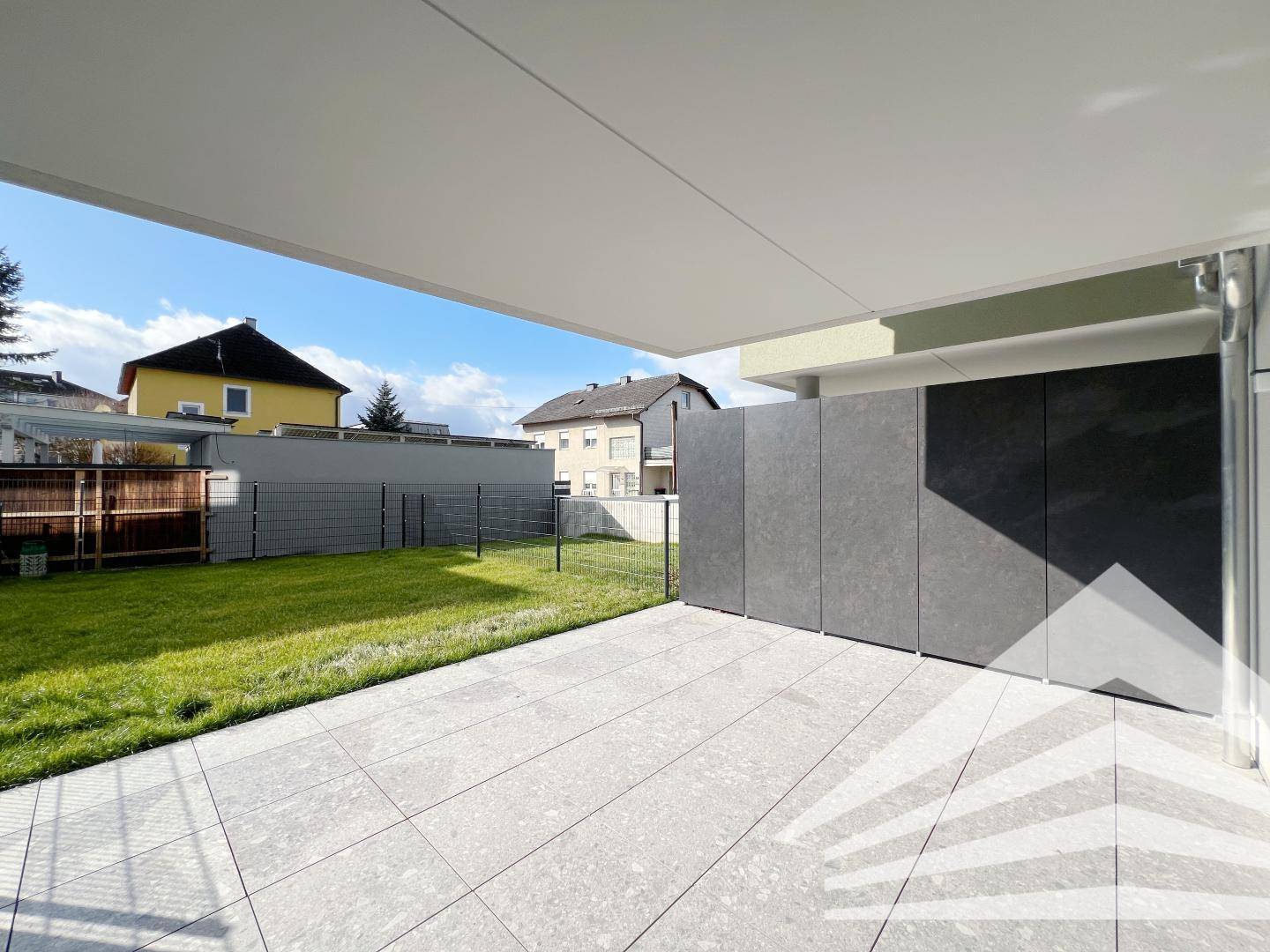 Überdachte Terrasse mit modernen Fliesen und Blick auf den Gartenbereich.