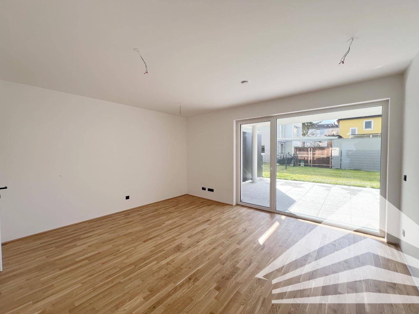 Heller Wohnraum mit Holzboden und großer Glasschiebetür zum Gartenbereich.