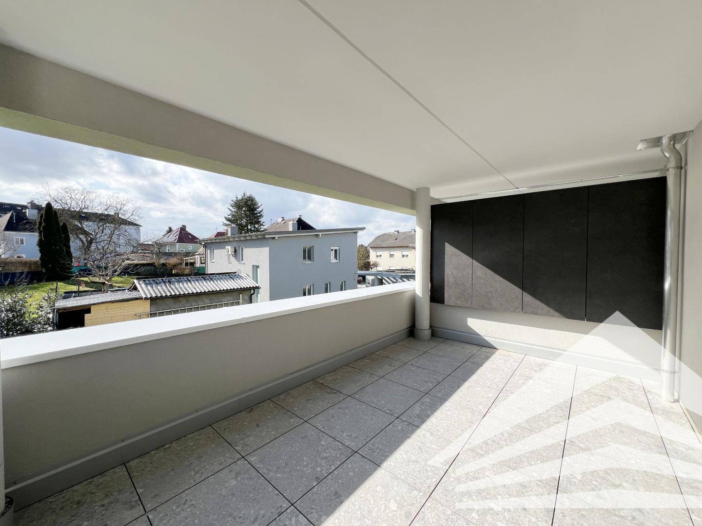 Geräumiger überdachter Balkon mit Fliesenboden und Blick auf die umliegende Wohnbebauung.