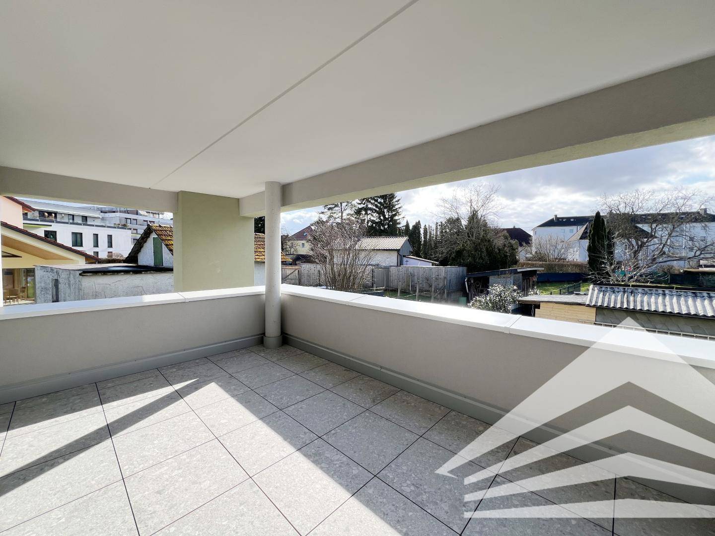 Heller, überdachter Balkon mit Fliesenboden und weitem Blick über die Nachbarschaft.