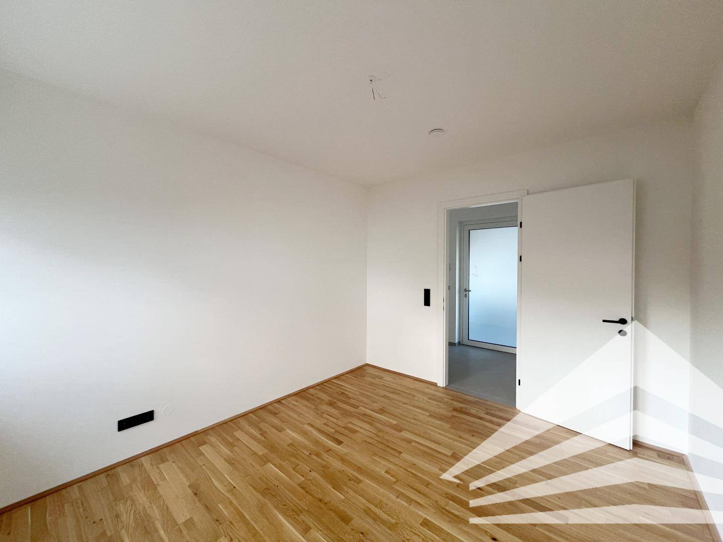Helles Schlafzimmer mit Parkettboden und weißer Tür, die zum Flur führt.