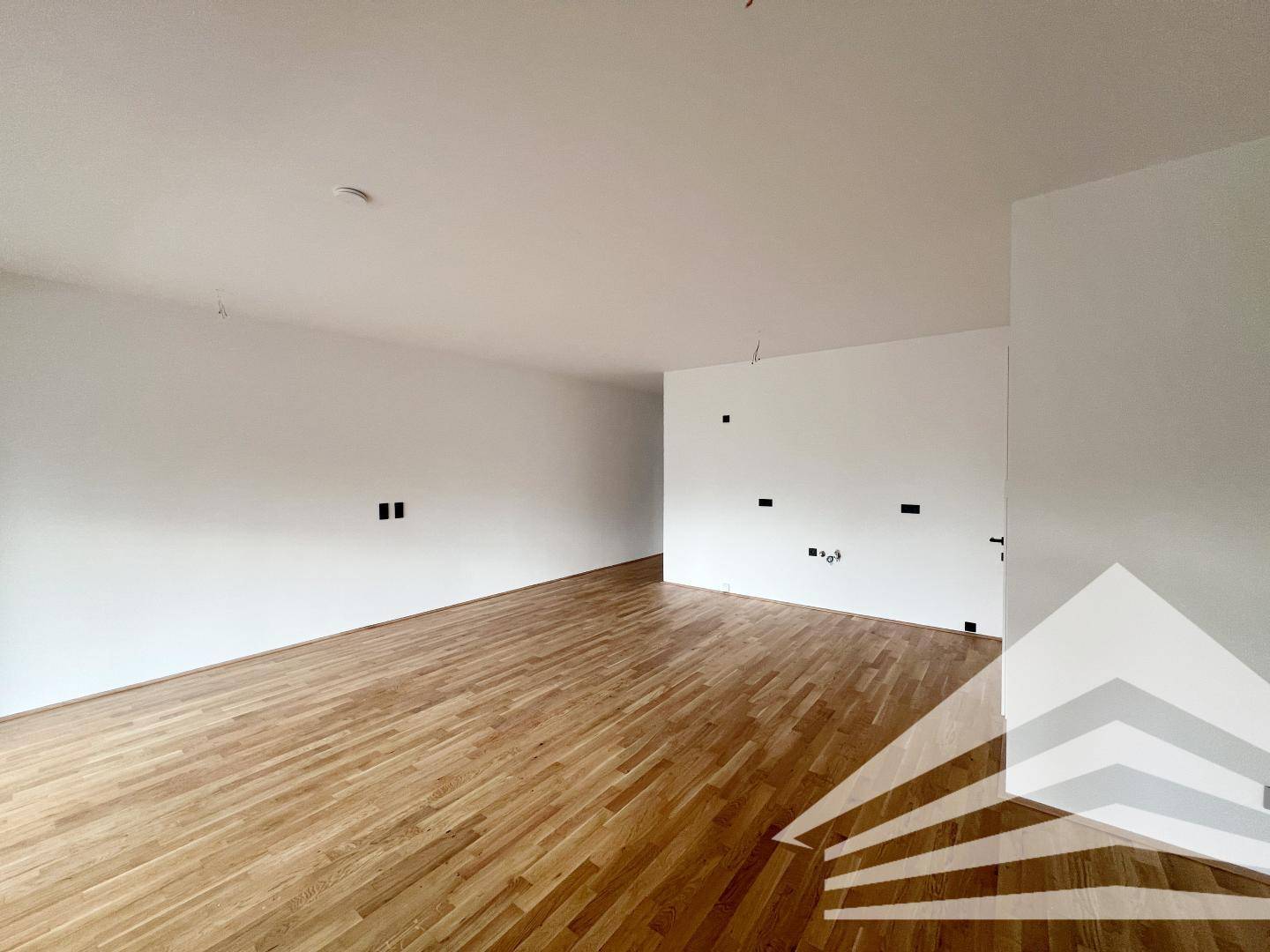 Geräumiges Wohnzimmer mit hellem Eichenparkett und weißen Wänden, bereit für die Einrichtung.