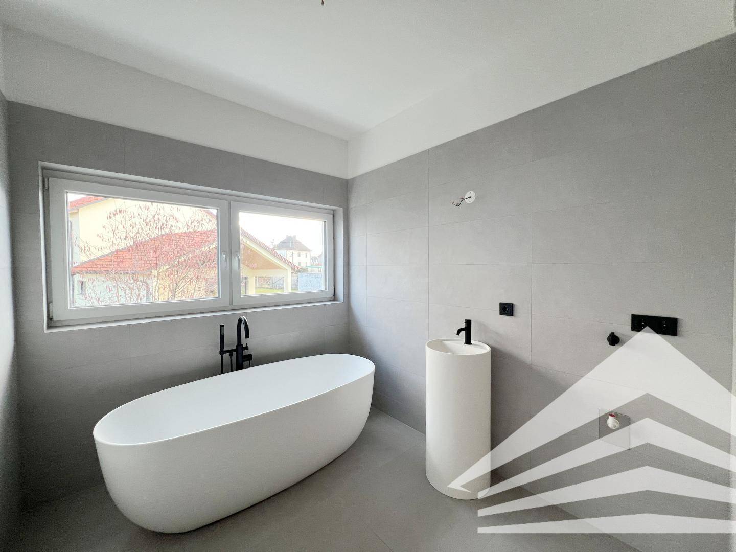 Elegantes Badezimmer mit freistehender Badewanne, modernem Waschtisch und großem Fenster.