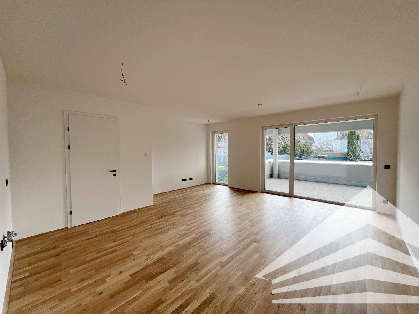 Helles, leeres Wohnzimmer mit Eichenparkettboden und Zugang zu einer großzügigen Terrasse.