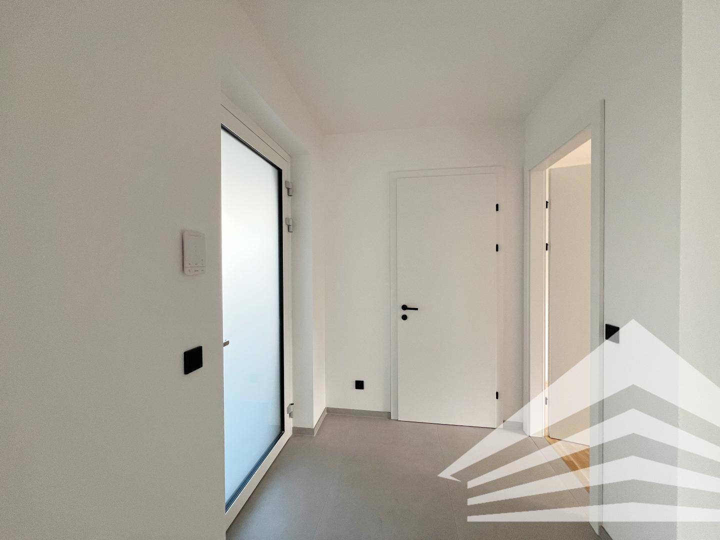 Heller Flur mit modernen Fliesen, weißer Tür und einem Fenster für natürliches Licht.