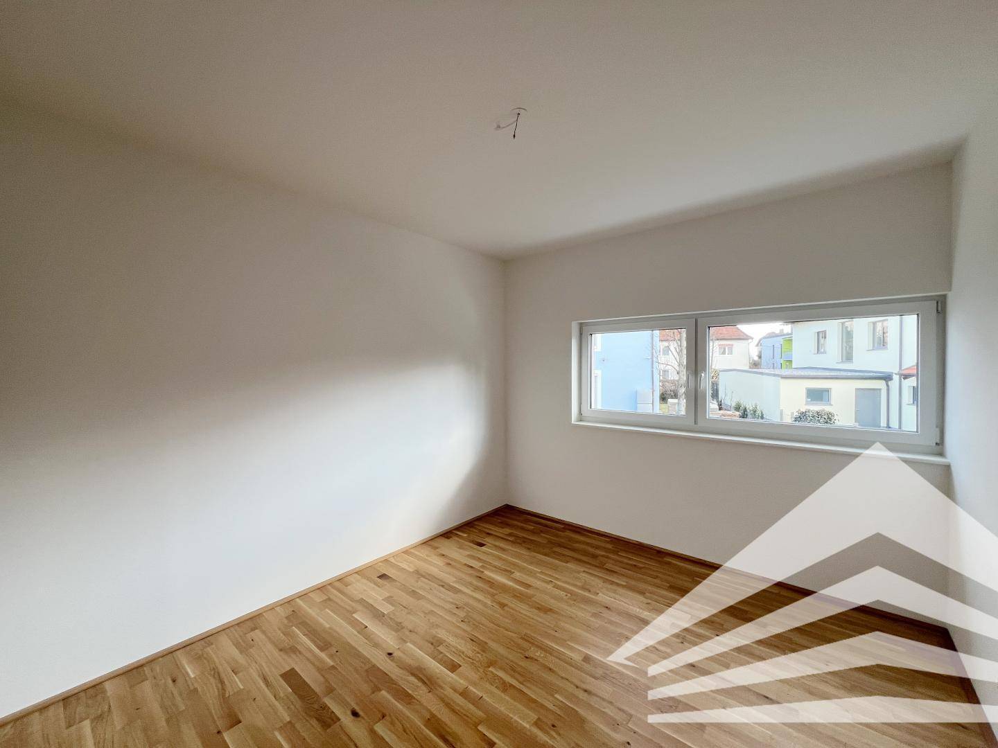 Lichtdurchflutetes Schlafzimmer mit Eichenparkett und Fenster, das einen Blick nach draußen bietet.