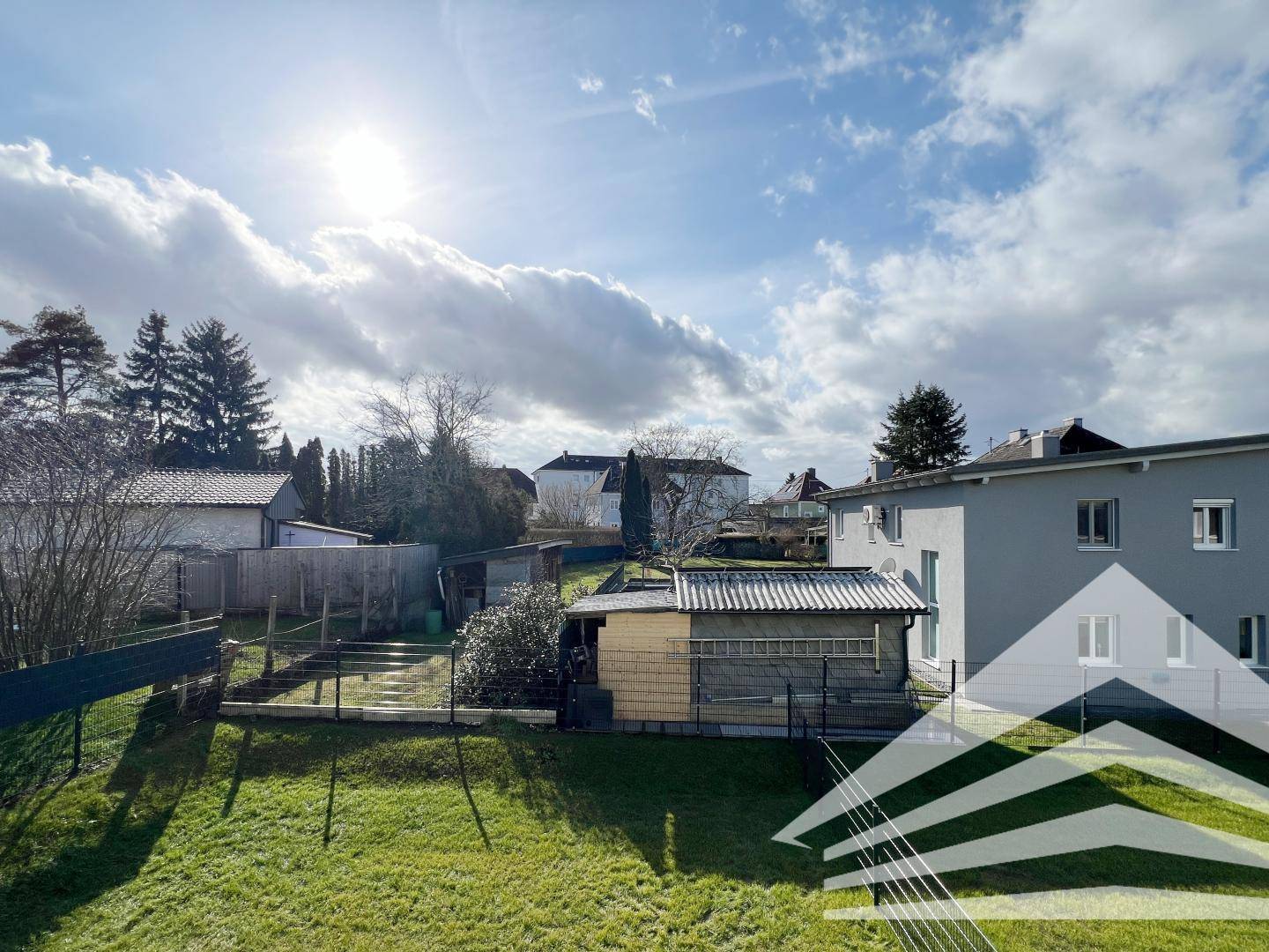 Weitläufiger Blick ins Grüne mit Gärten und umliegenden Häusern unter sonnigem Himmel.