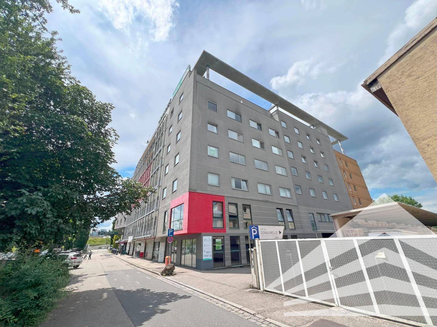 Straßenansicht des Gebäudes mit roter und grauer Fassade, Eingangsbereich und geparkten Autos.