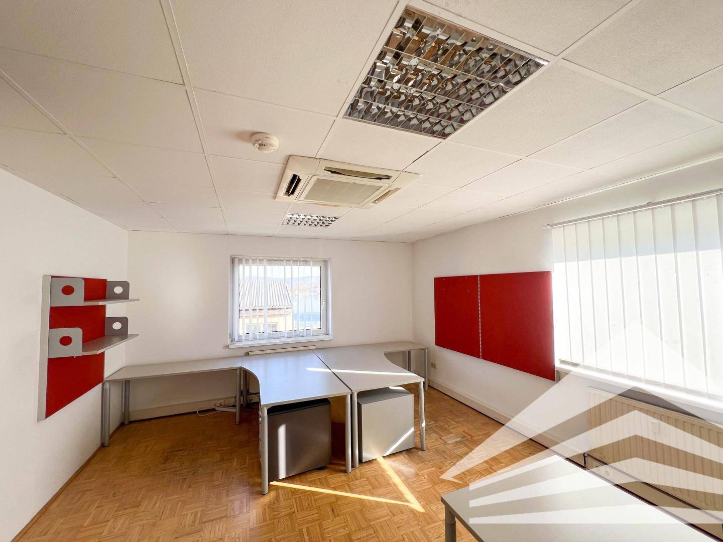 Kleineres Büro mit zwei Arbeitsplätzen, Schreibtischen, roten Akzenten und einem Fenster.