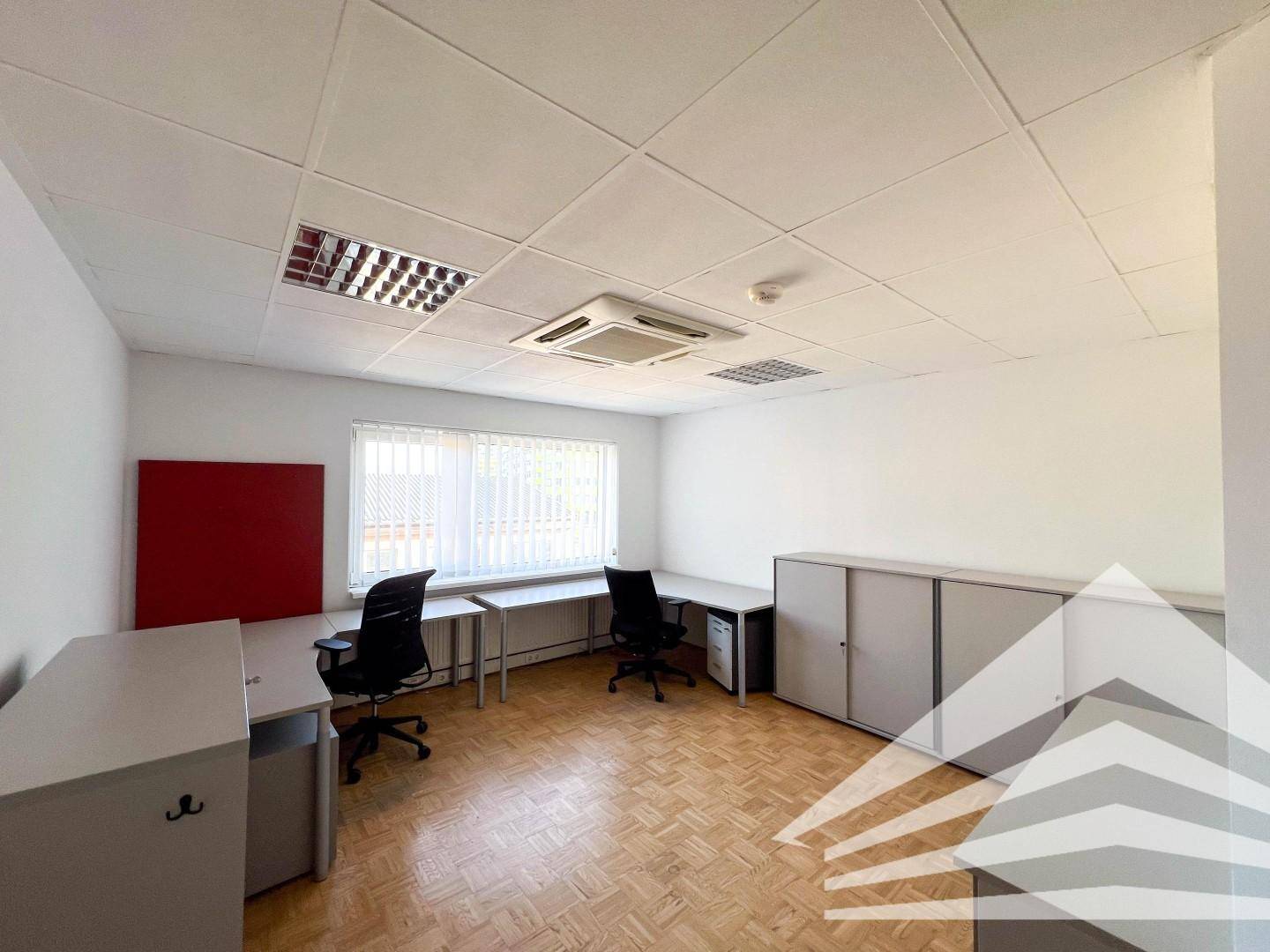 Büro mit zwei Arbeitsplätzen, Schreibtischen, Schränken, roter Akzentwand und Fenstern mit Jalousien.