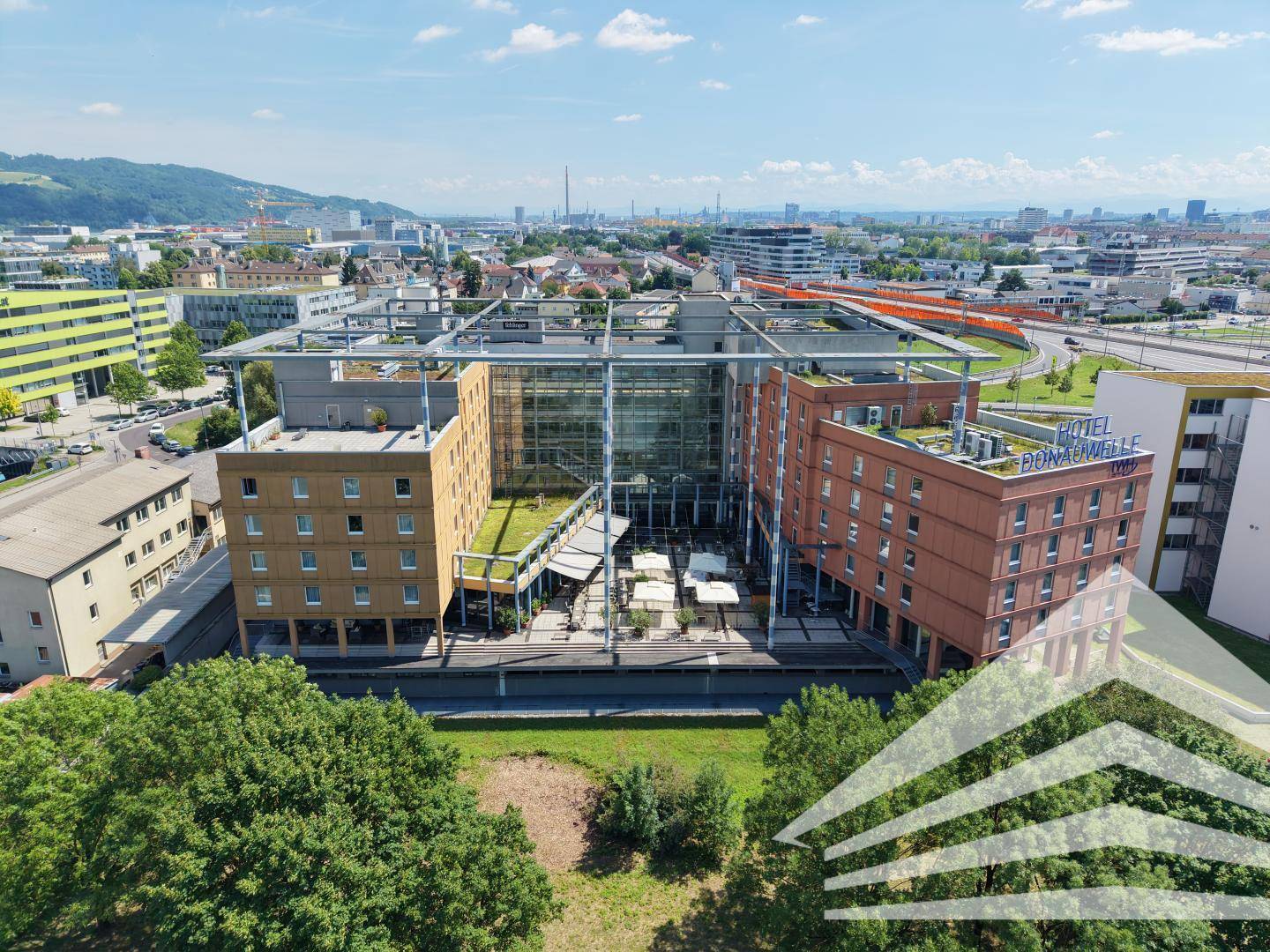 Luftaufnahme des Hotelkomplexes mit Innenhof, Glasfassade und umliegenden Gebäuden und Grünflächen.